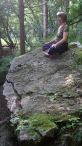 Nina in yoga position on a rock in the forest